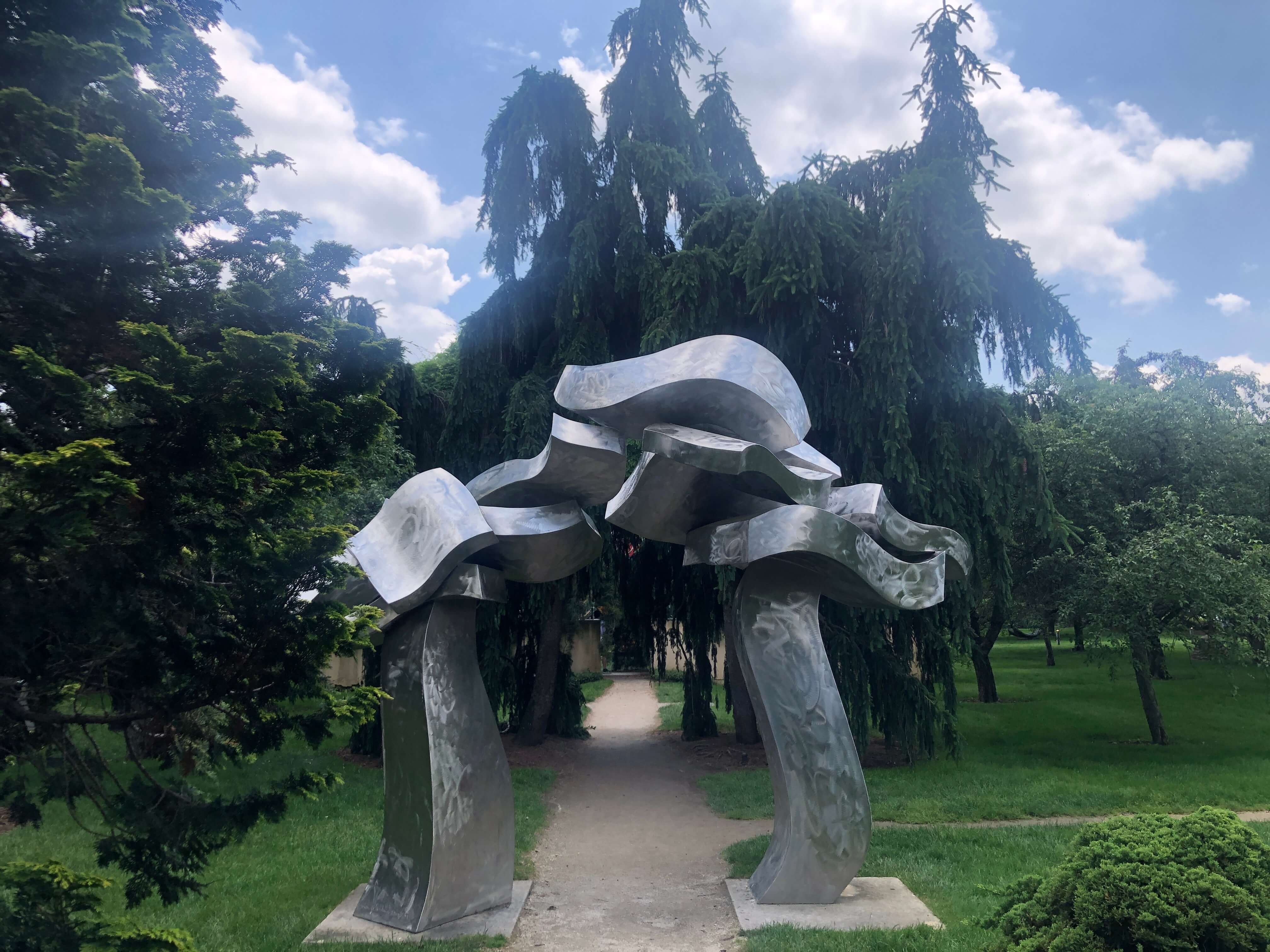 A stainless steel arch sculpture over a garden path