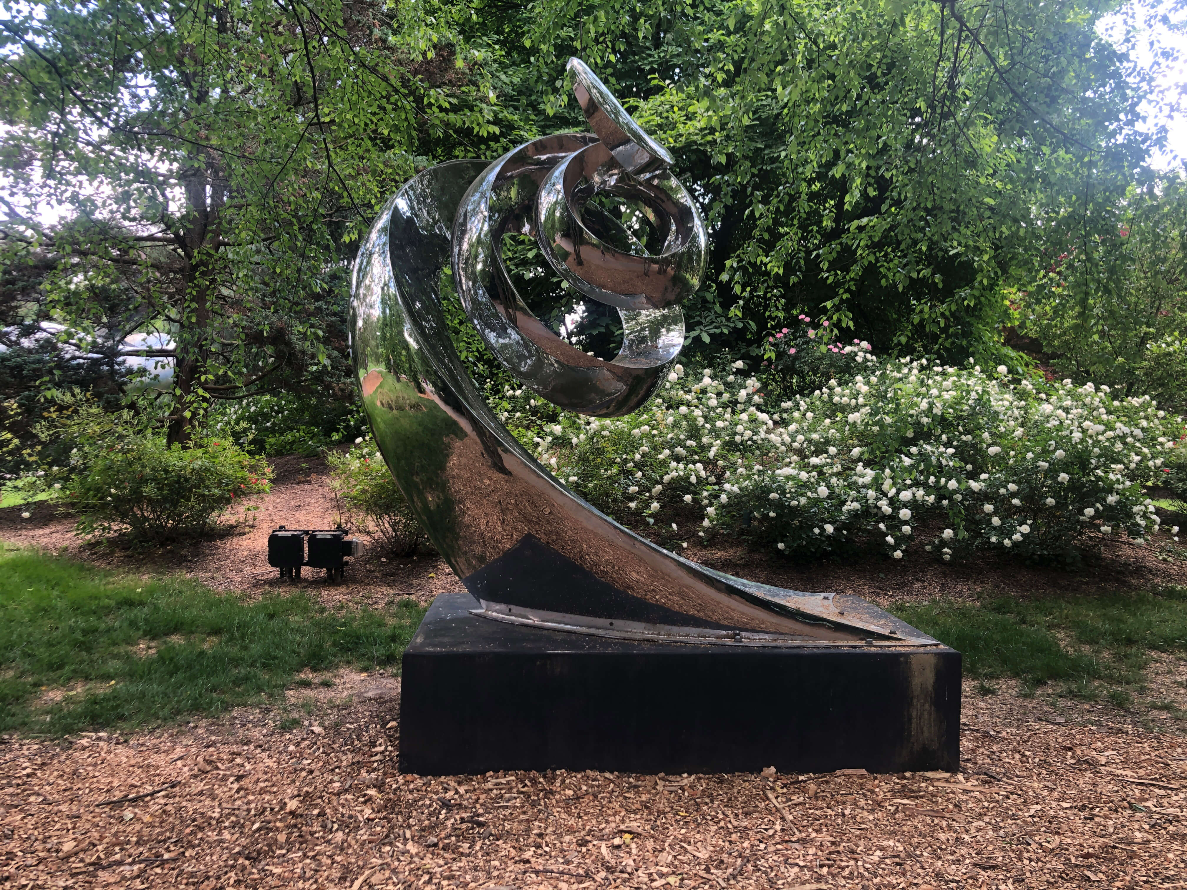 A polished steel spiral sculpture in a garden