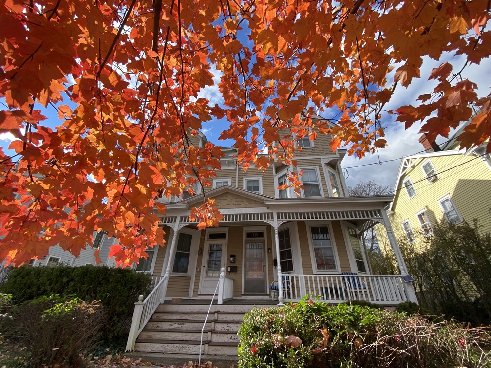 A clapboard Victorian house under a blazing orange maple