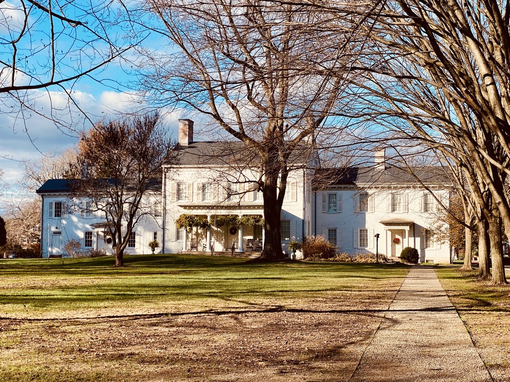 A white colonial mansion behind bare autumn trees